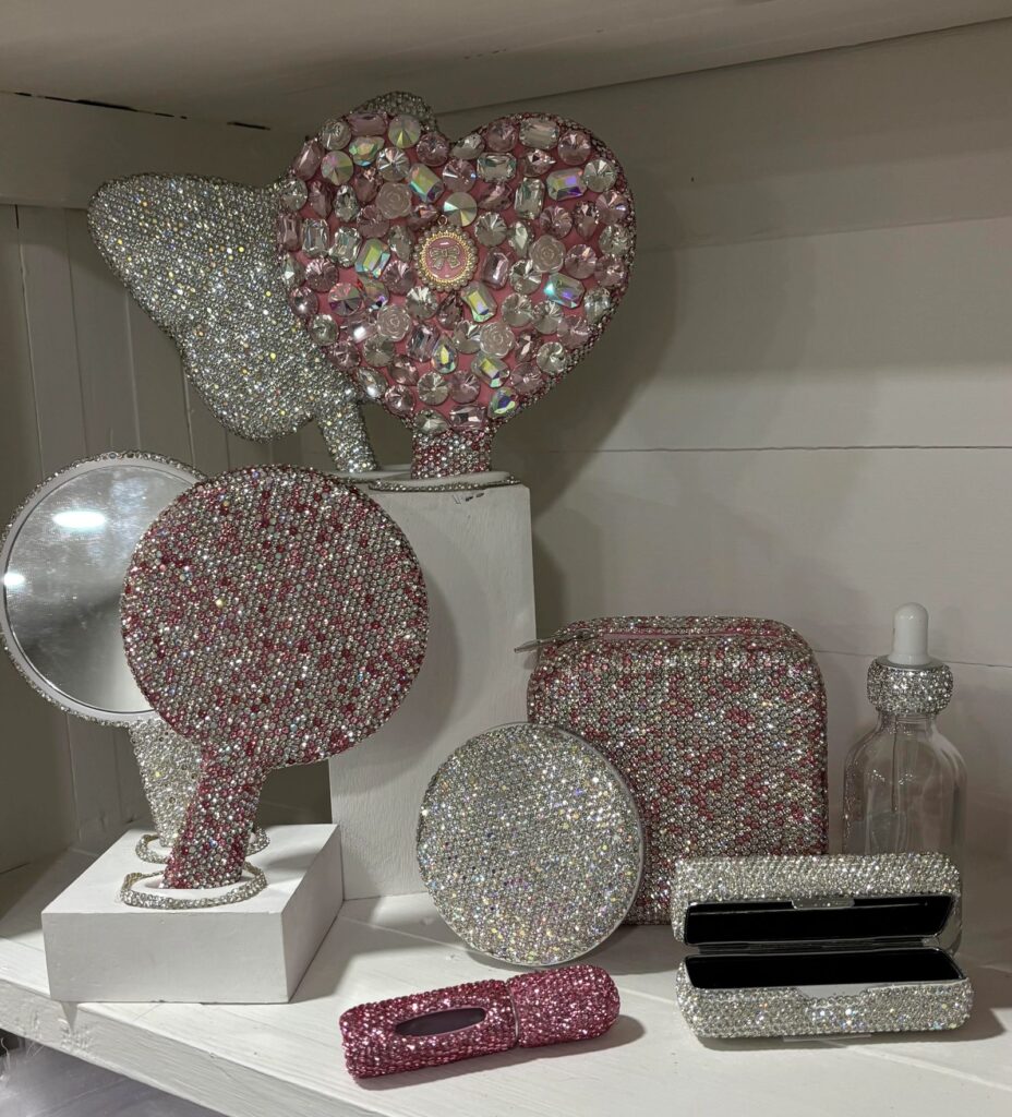 Rhinestone-covered compact mirrors, a cosmetic bag, and a perfume bottle on display at BlingBox